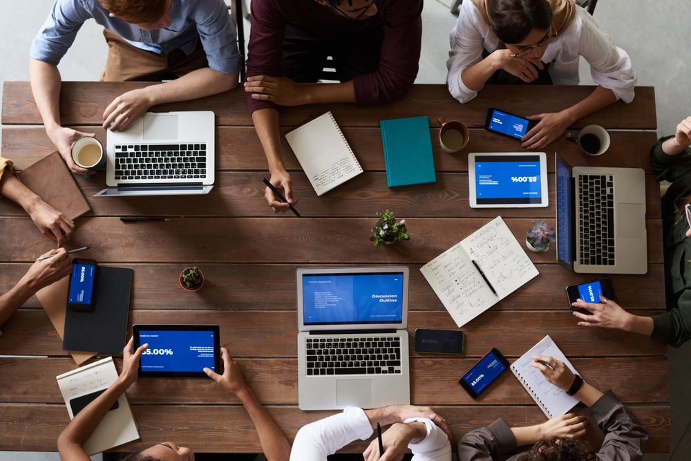 An overhead view of a working session, laptops and notebooks spread across a conference table