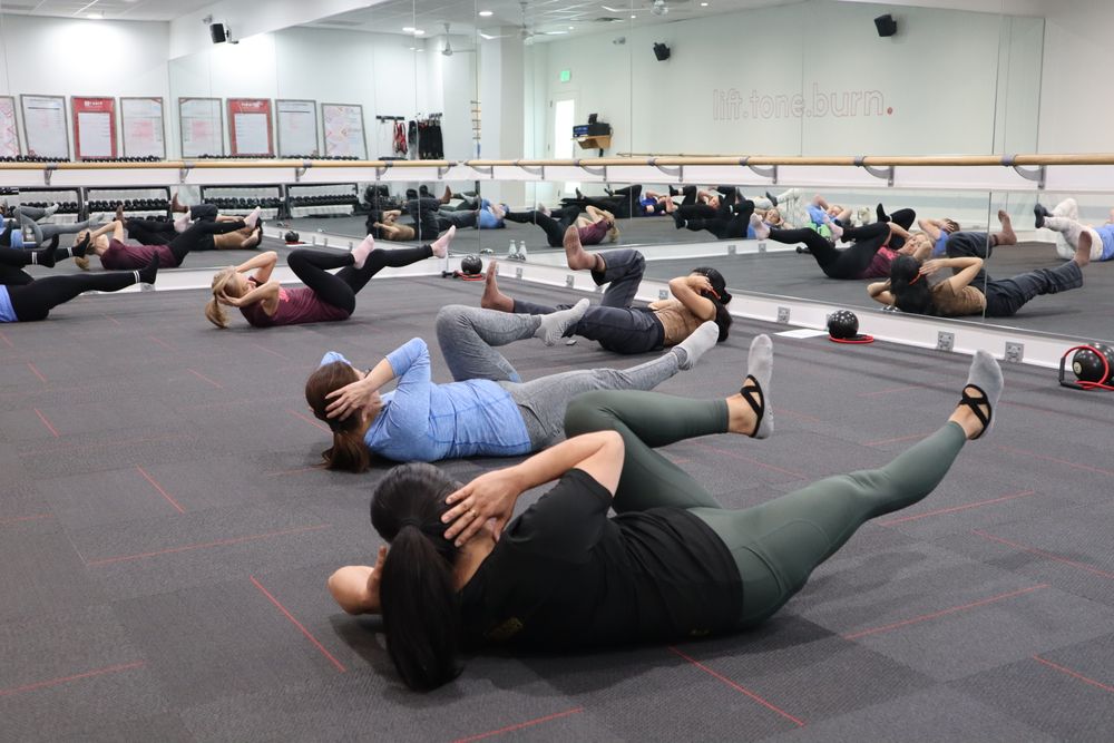 A boutique studio class mid-set on the floor of a mirrored barre room